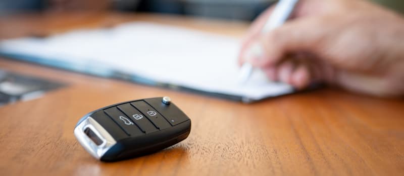 Someone filling out car logbook information with keys on table