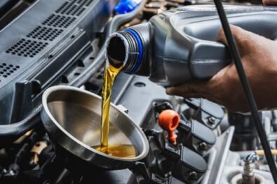 Car mechanic pouring engine oil into vehicle during doing car maintenance in garage