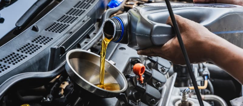 Car mechanic pouring engine oil into vehicle during doing car maintenance in garage